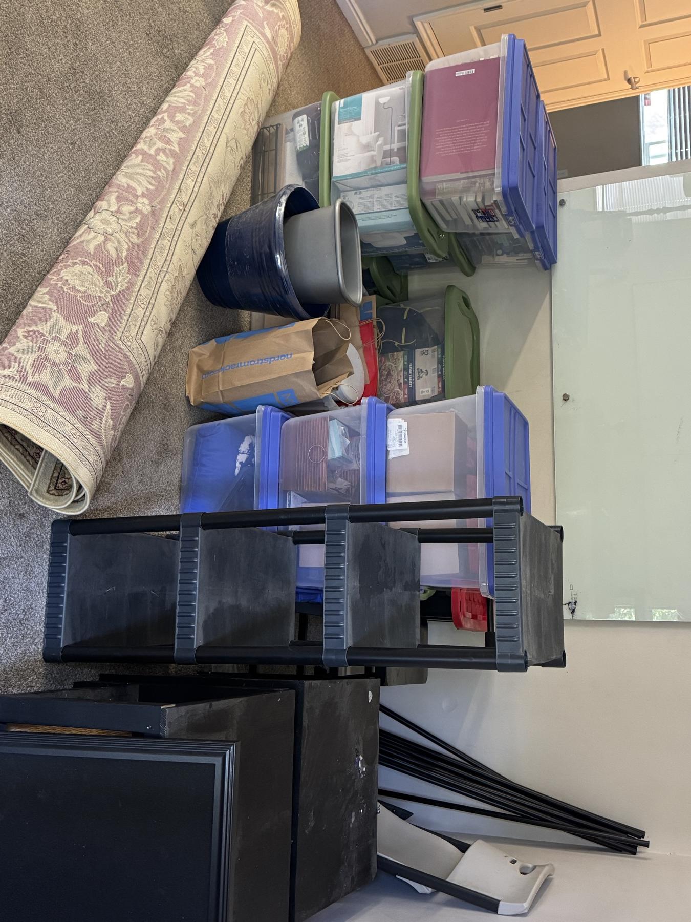 Household items staged before loading including bins, furniture, and rolled rugs